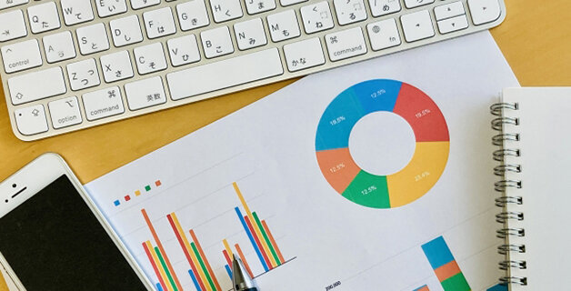 机の上のPC、スマホ、ノート、調査書